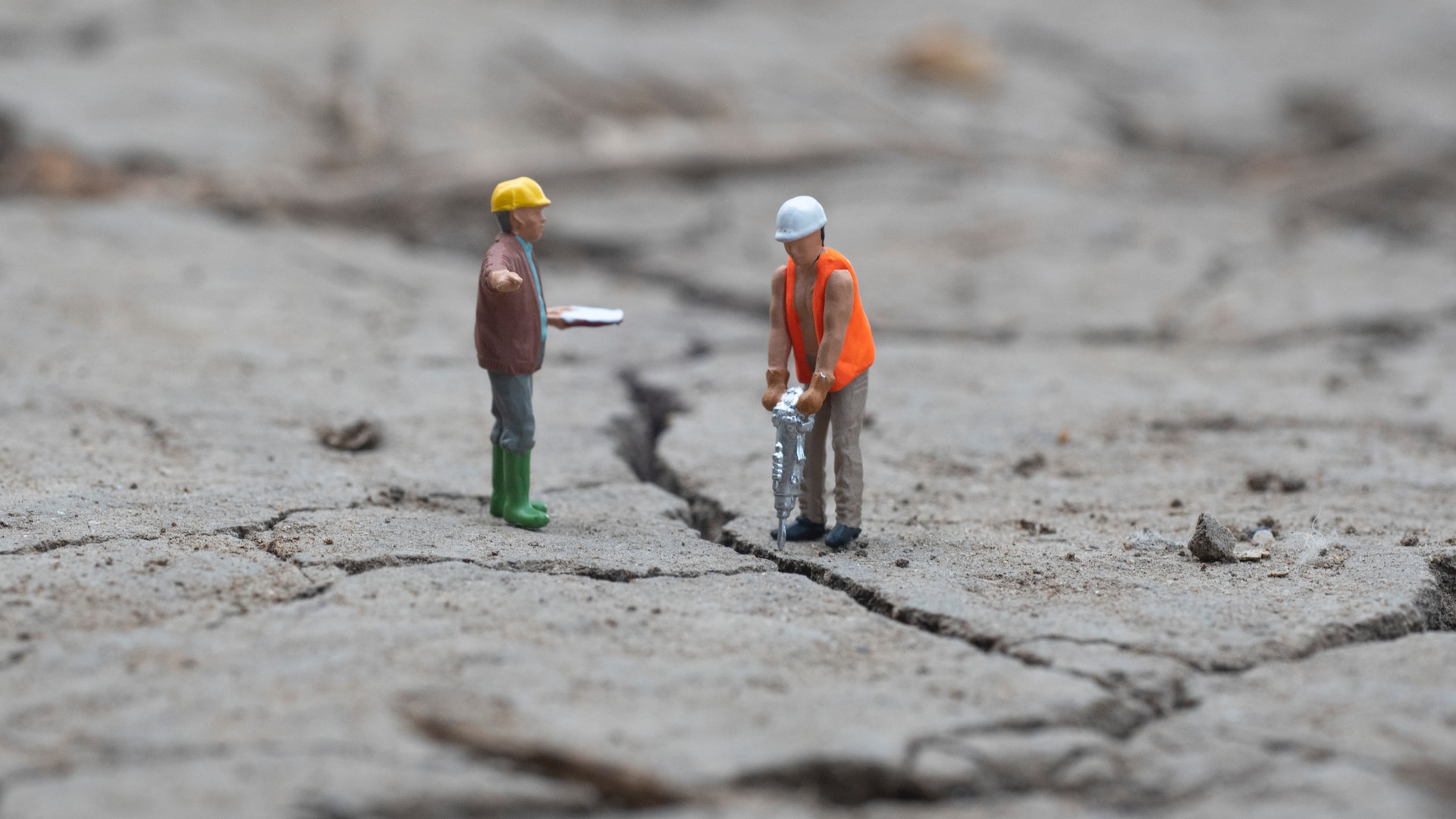 Two clay construction workers, one using a jackhammer to break up concrete.